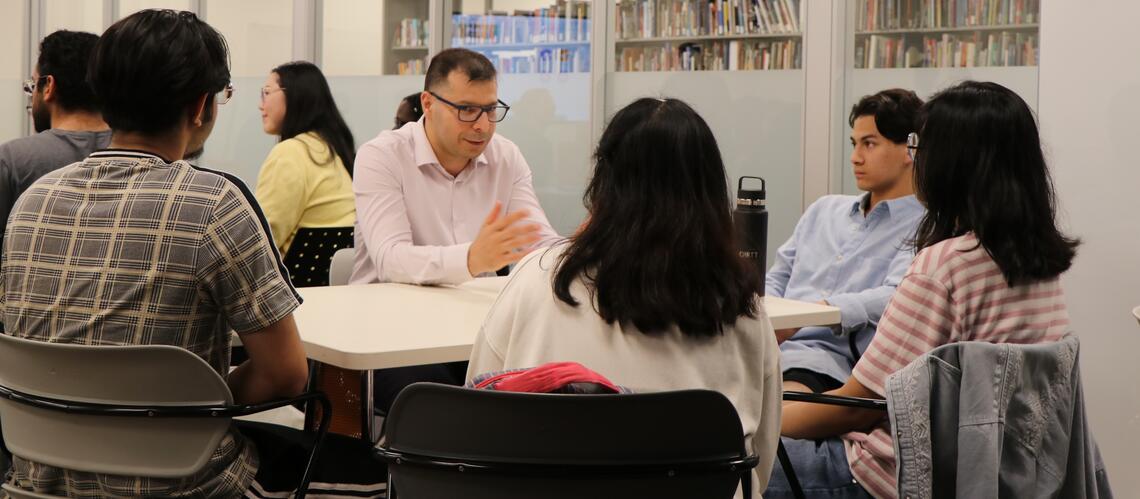 A man sits at a table surrounded by students